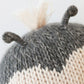 Close-up of the Cuddle + Kind Baby Ladybug, a collectible hand-knit baby animal made with gray and cream yarn, featuring two short, curled antennae and a tuft of cream yarn on top.