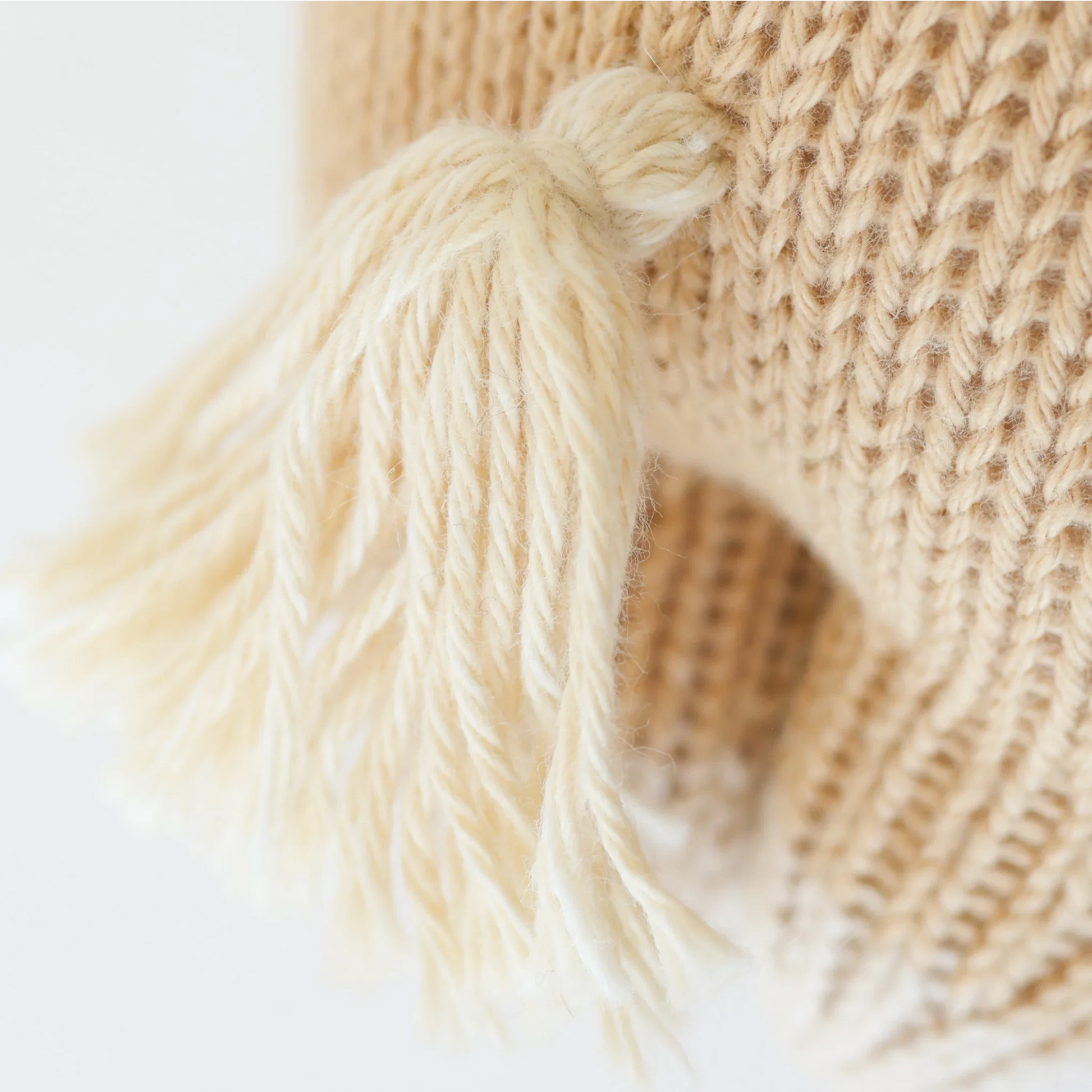 Close-up of a beige knitted item with a cream-colored tassel attached, showing detailed texture and fibers, meticulously crafted from handcrafted cotton yarn—perfect as an heirloom Cuddle + Kind Baby Pony or a soft baby toy.