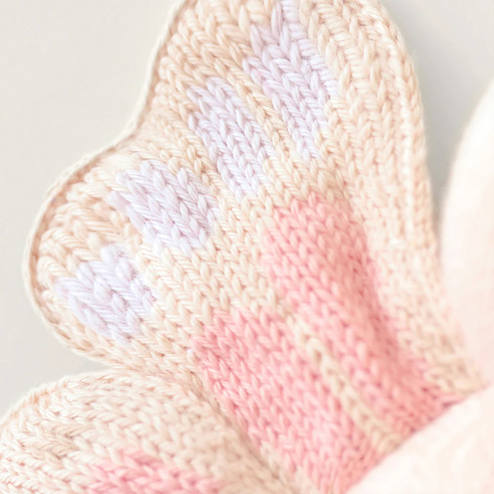 Close-up of Cuddle + Kind’s Baby Butterfly - Petal Pink: an heirloom-quality, hand-knit fabric shaped like a flower petal in soft pink and cream tones—ideal for collectible creations or hand-knit baby decor.
