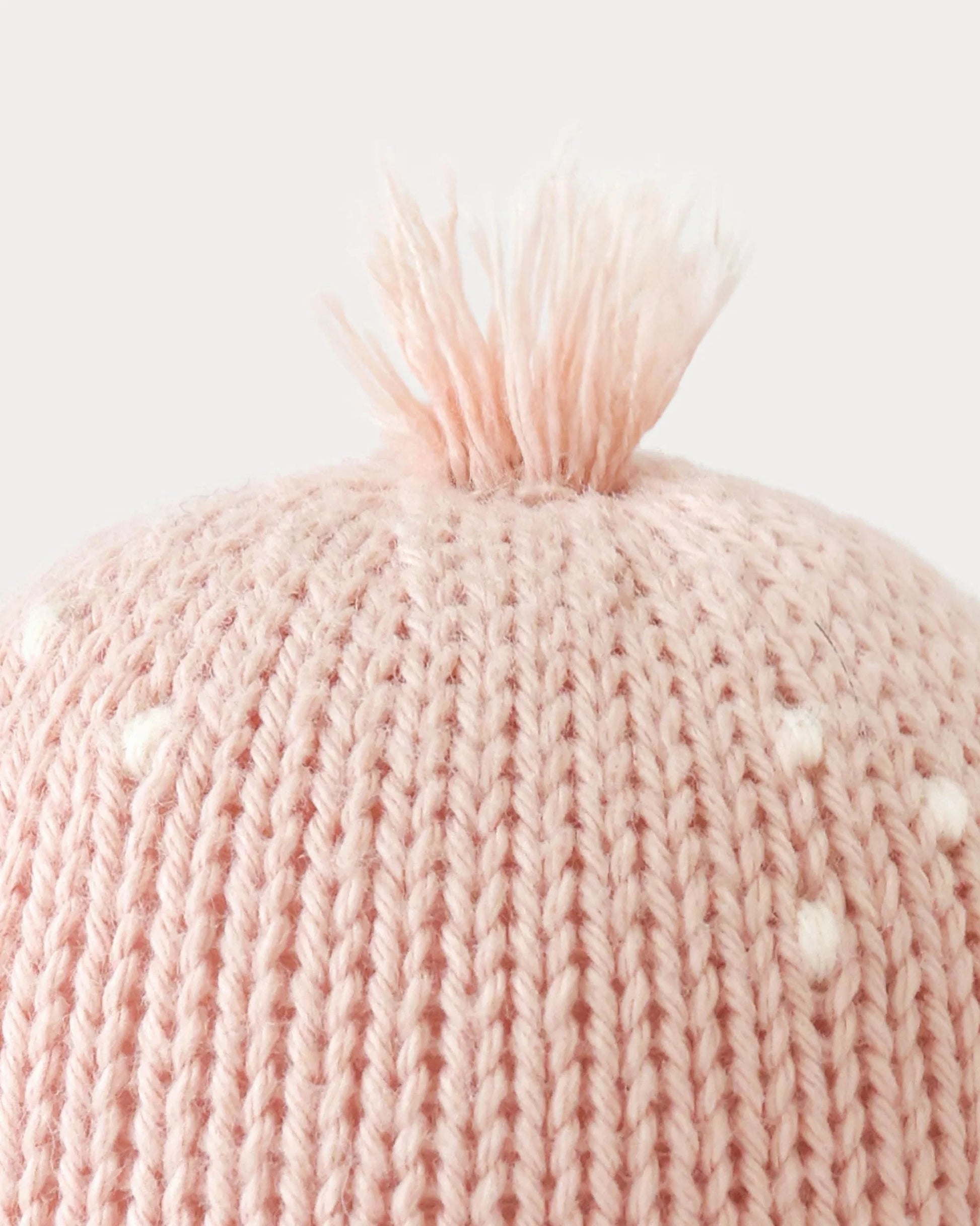 Close-up of the top of the Baby Octopus - Soft Coral Pink hat by Cuddle + Kind, crafted from soft Peruvian cotton yarn in a gentle pink hue, featuring charming white dots and a small tuft of yarn at the crown against a plain background.