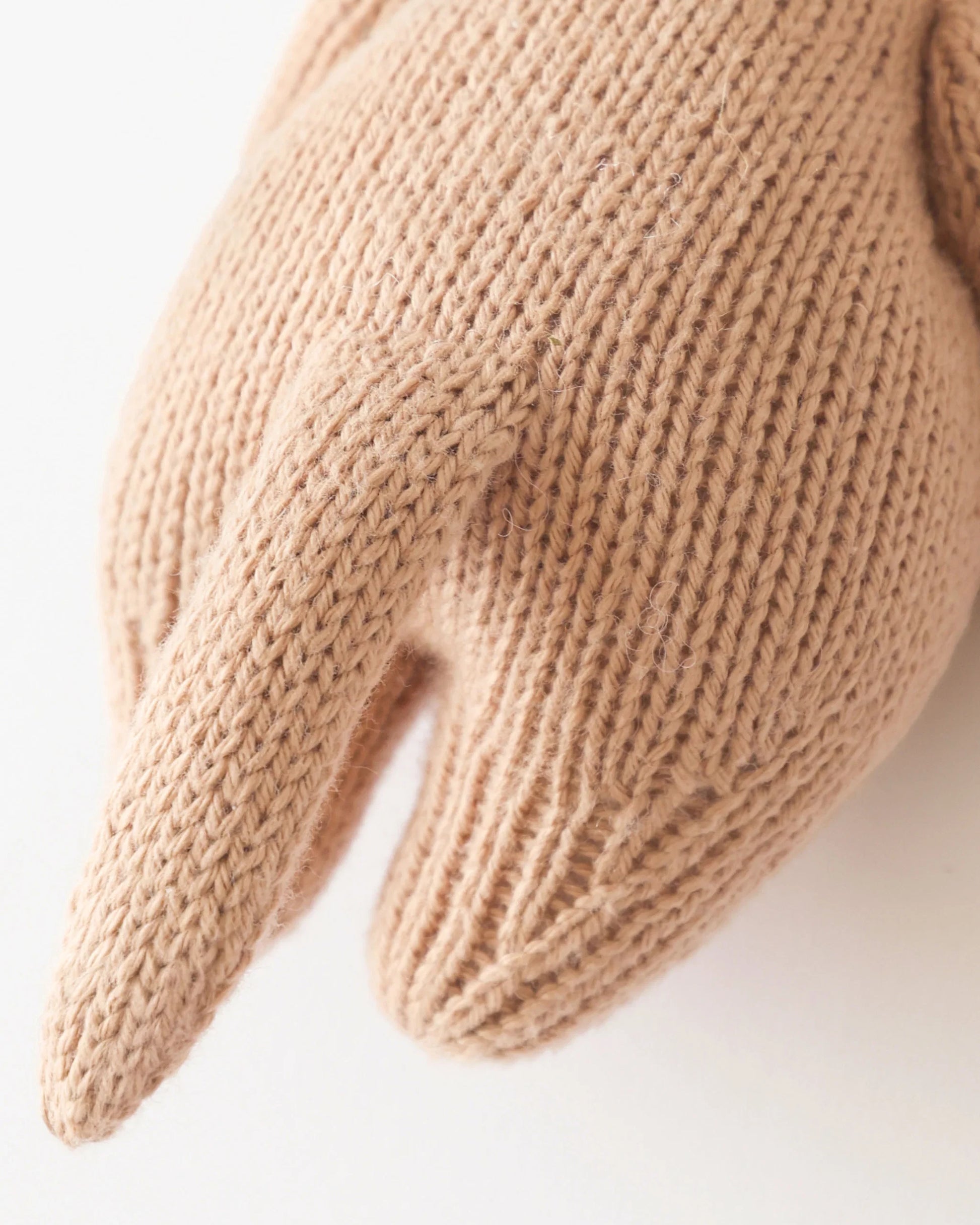 Close-up of a knitted object resembling the back and tail of a small animal, lovingly crafted in beige yarn from handcrafted Peruvian cotton to create Cuddle + Kind’s heirloom-quality Baby Otter.