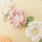 Close-up of the knitted fabric on Flora the Duckling, Mauve - Regular 20" by Cuddle + Kind, featuring crocheted pink and white wildflowers with green leaves sewn onto a soft light yellow background.