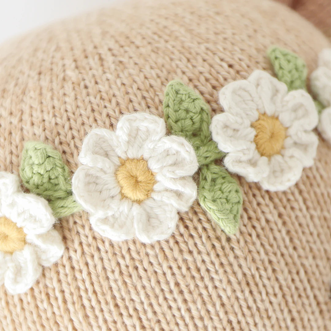 Close-up of the Charlotte the Dog - Little 13" by Cuddle + Kind, featuring beige knitted fabric with charming white and yellow embroidered flowers and green leaves for a garden-inspired look.