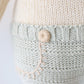 Close-up of Sawyer the Lion - Regular 20" by Cuddle + Kind shows cream and light gray knitted fabric, a round button, and beige stitching—a thoughtfully textured plush that's perfect as a birthday gift.
