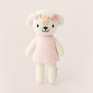 Tiny Charlotte the Dog by Cuddle + Kind is a hand-knit plush from the Tiny Collection, dressed in a pink dress and flower crown, shown standing upright against a simple light background. Perfect for collectors and snuggles.