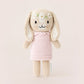 Tiny Hannah the Bunny Blush by Cuddle + Kind is a fair trade, hand-knit doll with long ears, a pink dress, and a flower crown, standing against a plain light background.