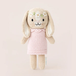Tiny Hannah the Bunny Blush by Cuddle + Kind is a fair trade, hand-knit doll with long ears, a pink dress, and a flower crown, standing against a plain light background.