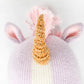 Close-up of Zoe the Unicorn - Little 13" by Cuddle + Kind, a magical knitted toy with a gold horn, pink mane, and purple ears set against a plain background.