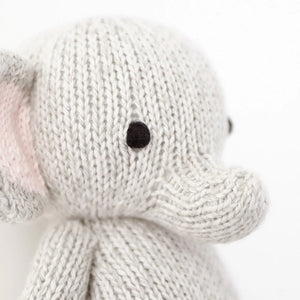 Close-up of Cuddle + Kind’s Baby Elephant, an heirloom-quality toy hand-knit from soft Peruvian cotton yarn. Features visible include its ear, trunk, and black stitched eye, set against a plain white background.
