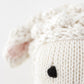 Close-up of the Baby Lamb by Cuddle + Kind, featuring handcrafted cotton yarn, a soft white head, pink ear detail, and black stitched eye—an adorable plush for any collector.