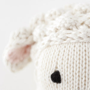 Close-up of the Baby Lamb by Cuddle + Kind, featuring handcrafted cotton yarn, a soft white head, pink ear detail, and black stitched eye—an adorable plush for any collector.