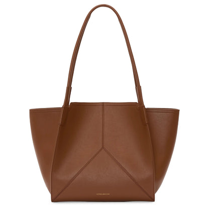 The Victoria Tote by Victoria Beckham is a brown leather bag with long shoulder straps and subtle stitching, Italian crafted and suede lined, shown against a white background.