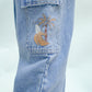 Gingersnaps Boys' Loose Cargo Pant Denim features a banana print and wide-leg cargo style in light blue, with an embroidered design on the pocket showing a palm tree, wave, and small white detail.