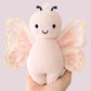 A hand holds the Cuddle + Kind Baby Butterfly - Petal Pink, an heirloom-quality plush toy with embroidered eyes, a smiling mouth, and patterned wings—a unique collectible for fans of hand-knit baby animals.