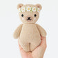 A hand holds the Baby Honey Bear Ivory Floral by Cuddle + Kind—an heirloom-quality, hand-knit beige teddy bear with a white and yellow flower crown and simple embroidered face.