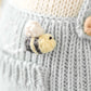 Charlie the Honey Bear by Cuddle + Kind, Regular 20", features a small knitted bee attached to light gray knit fabric, adding a charming honey bee detail to this adorable plush companion.