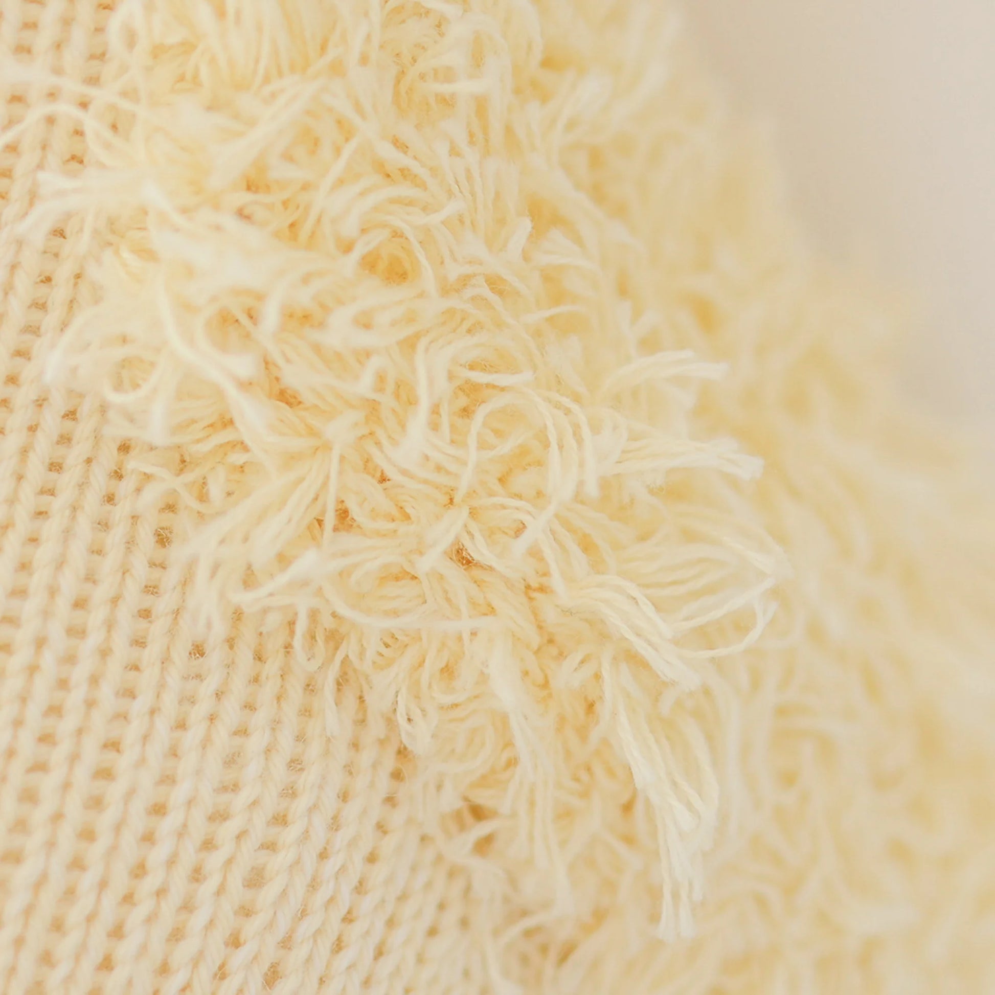 Close-up of Flora the Duckling Mauve - Little 13" by Cuddle + Kind shows cream-colored textured knit with shaggy, frayed yarn, evoking wildflowers in a spring meadow.