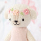 Tiny Charlotte the Dog from Cuddle + Kind's Tiny Collection is a hand-knit, cream-colored stuffed animal wearing a pink dress and a flower crown embroidered with pink and peach yarn.