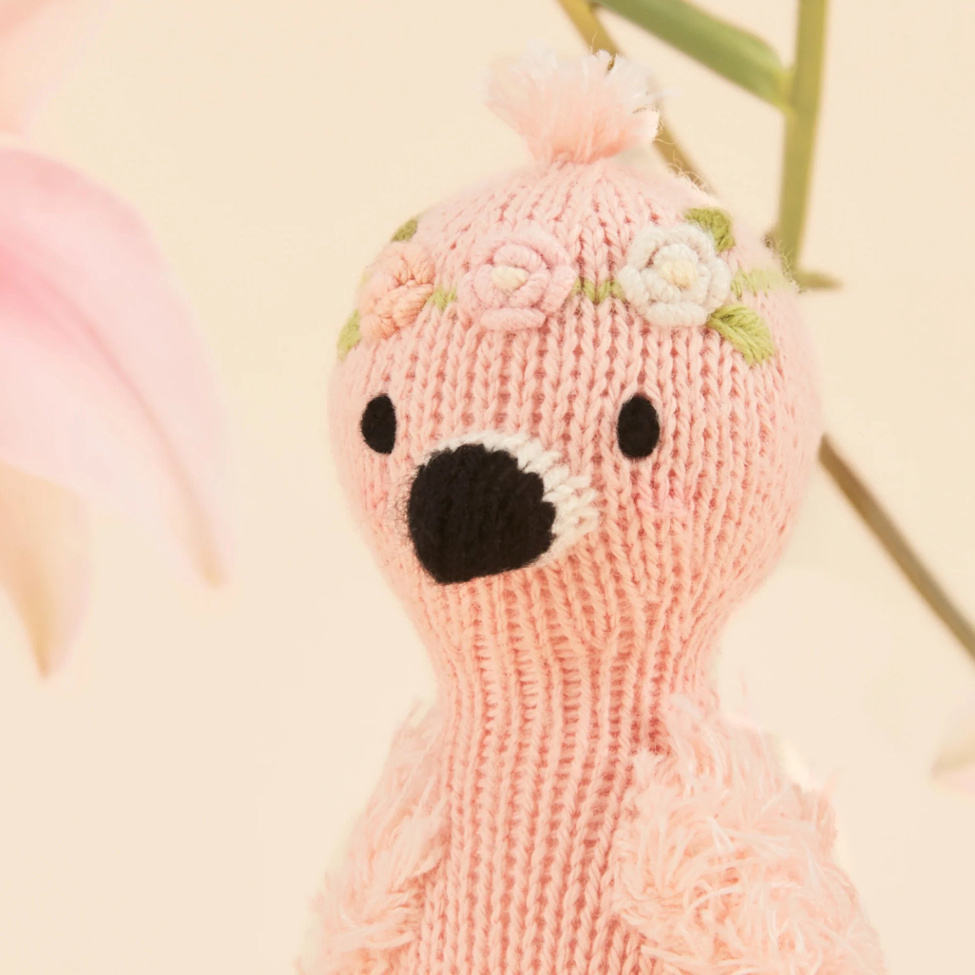 Tiny Penelope the Flamingo by Cuddle + Kind is a hand-knit toy with embroidered flowers on her head and a black beak, shown against a soft, light background—crafted with care.