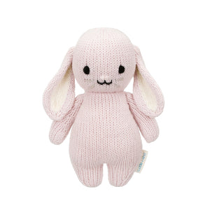 Here’s a rewritten version using your product data: The Lilac Bunny - Baby 7" by Cuddle + Kind is a pale pink hand-knit stuffed bunny, featuring long floppy ears, black eyes, and a gentle smile, shown against a white background. Crafted from the softest Peruvian cotton yarn, this heirloom-quality bunny makes a cherished keepsake and perfect companion for playtime.