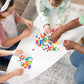 Four children sit around a white table on a grey carpet, assembling Plus Plus Tube - 240 Piece Neon Mix—colorful STEM toys that inspire creative play and help develop fine motor skills.