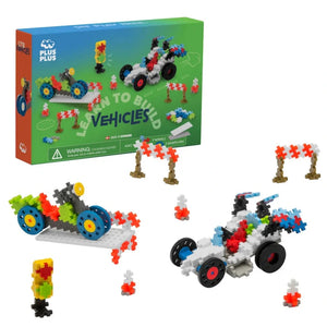 The Plus Plus Learn to Build - Vehicles set features assembled race cars, traffic barriers, and small structures, shown with the product box in the background.
