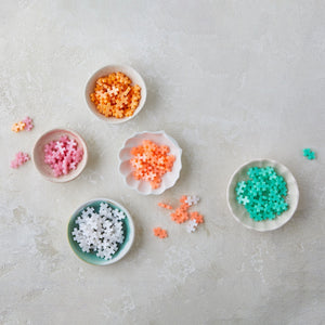 Five small bowls filled with Plus Plus Tube - 240 Piece - Pearl Mix puzzle pieces, arranged on a light textured surface with some loose pieces nearby—ideal for creative play and building fine motor skills.