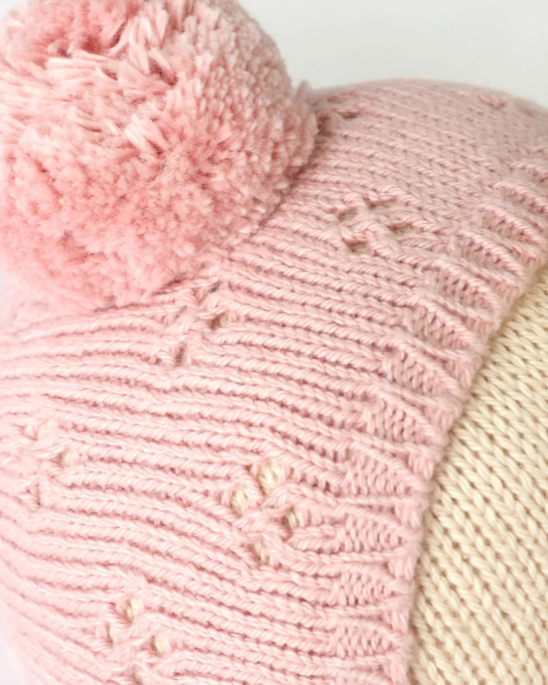 Close-up of the “My First Baby” pink hand-knit hat by Cuddle + Kind, featuring a pom-pom on top and a subtle star pattern, crafted from natural cotton and displayed on a mannequin head.