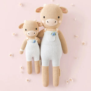 Asher the Cow by Cuddle + Kind comes in a regular 20" size, wearing white overalls with blue flowers. Set on a light pink background with white blooms, this plush cow inspires kindness and makes a sweet gift for any occasion.
