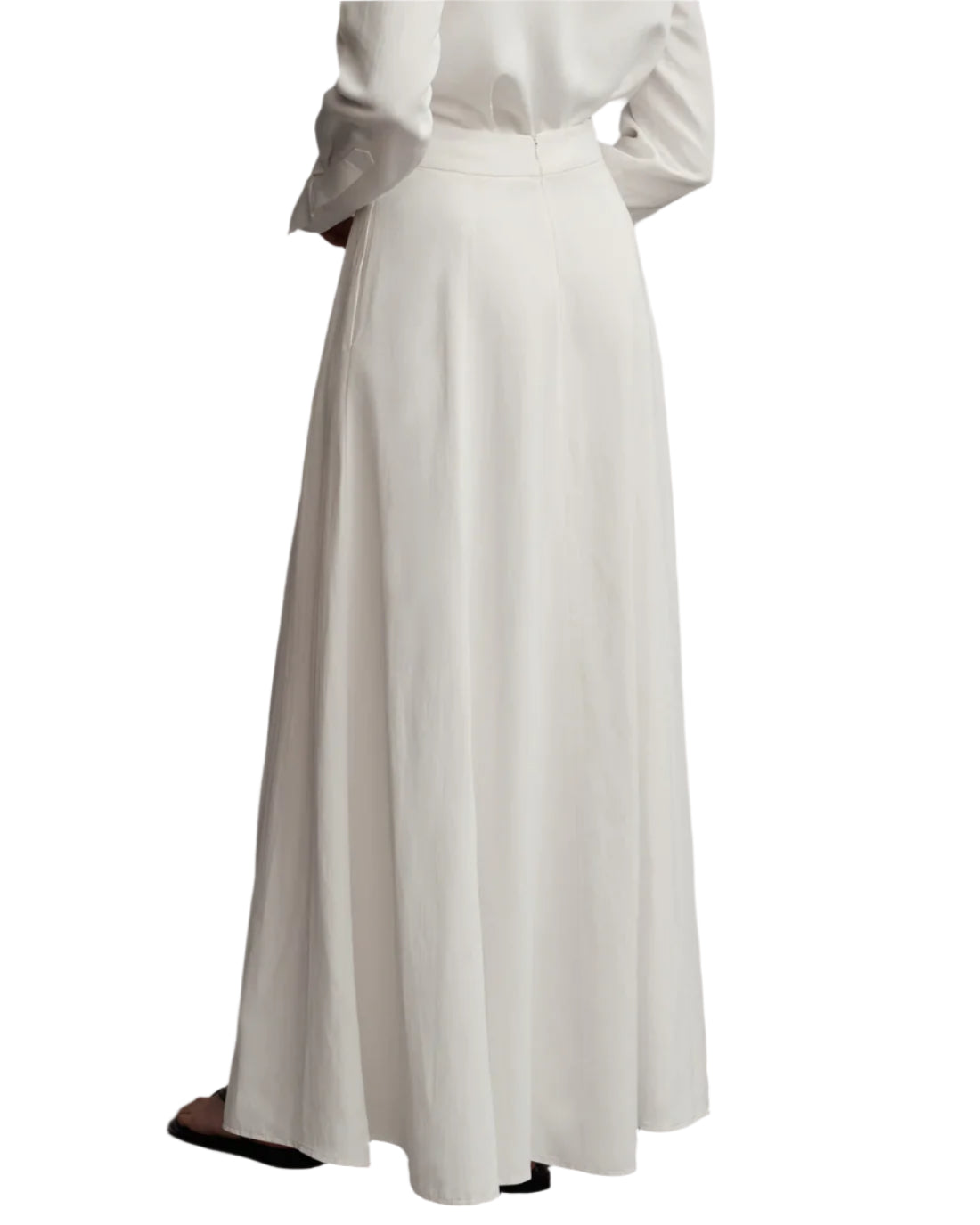 A person is seen from the back wearing the TWP Kennedy Skirt Coated in a maxi style, paired with a long-sleeved white top made of coated viscose linen.