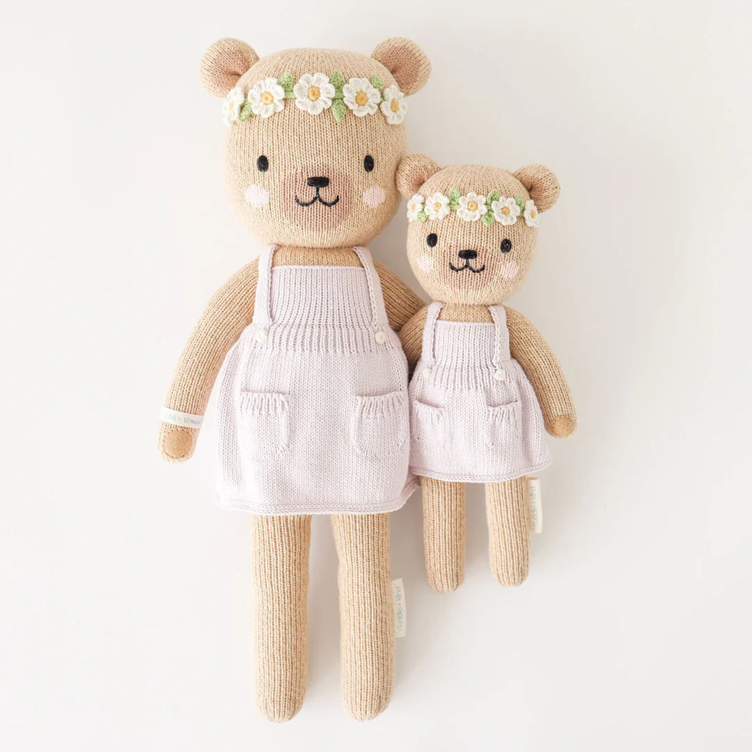 Olivia the Honey Bear by Cuddle + Kind (Regular 20") wears a floral headband and pale apron, gently holding the hand of a smaller bear. Both plush toys sit against a plain white background, ready for adventure.