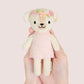 A hand is holding a Cuddle + Kind Tiny Charlotte the Dog, a fair trade hand-knit doll dressed in a pink dress with flower embroidery on its head.