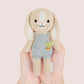 A hand holds Tiny Henry the Bunny, a hand-knit doll in light blue overalls with a carrot patch, from the Cuddle + Kind Tiny Collection.