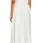 A woman in the Eliza Dress by Brandon Maxwell, featuring a white, sleeveless, V-neck midi design crafted from an Italian silk blend with subtle patterns, stands facing away. She completes her look with silver high heels, embodying essential resort-season elegance.