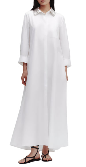 Against a plain background, a person wears the TWP Jennys Gown with Crystal Collar, made from luxurious Italian cotton shirting. They complete their look with black sandals, adding elegance.