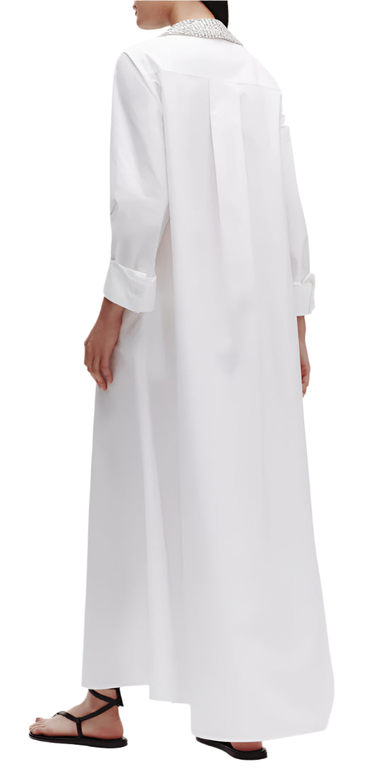 A person is wearing the TWP Jennys Gown with Crystal Collar, crafted from Italian cotton shirting, paired with black sandals and standing sideways.