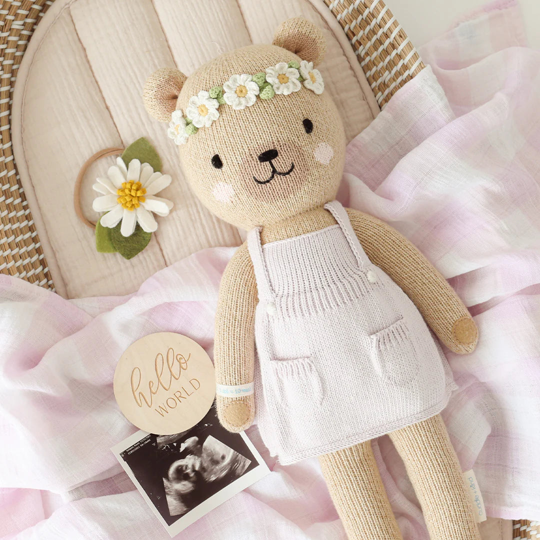 Charlotte the Dog – Little 13" by Cuddle + Kind, wearing a flower crown and light apron, rests on pink cloth beside a daisy, “hello world” sign, and ultrasound photo—celebrating new life and floral love.