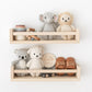 Two wooden wall shelves display heirloom-quality treasures against a white wall: a hand-knit Baby Lion from Cuddle + Kind, collectible wooden stacking toys, a "hello world" sign, a beaded toy, and small brown shoes.