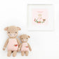 Two "Ava the Cow Powder Pink - Little 13"" plush dolls by Cuddle + Kind in pink overalls with embroidered strawberries sit together beneath a "Friendship grows everywhere" print—an adorable gift for someone special.