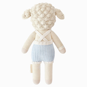 Benjamin the Lamb - Little 13" by Cuddle + Kind is a knitted plush toy resembling a sheep, dressed in light blue overalls with white straps and shown from the back against a plain white background—an adorable stuffed animal and perfect gift for kids.