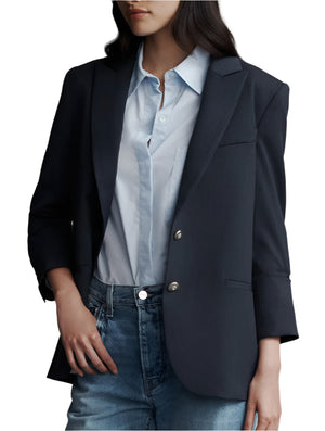 A person in a TWP Boyfriend Blazer styled over a light blue collared shirt and jeans effortlessly showcases chic fashion with its slightly oversized silhouette.