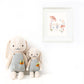 Two Henry the Bunny dolls by Cuddle + Kind, each 20" tall and dressed in gray overalls, sit side by side like best friends beneath a framed bunny illustration with mushrooms and flowers on a white wall.