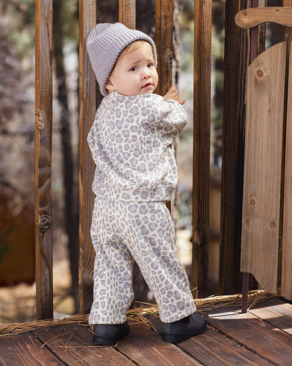 A toddler wearing the Rylee & Cru Baby Girls’ and Girls’ Oversized Sweatshirt stands on a wooden deck, looking back over their shoulder.