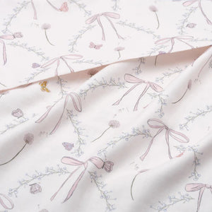 Close-up of Gooselings' Bows & Butterfly Kisses Swaddle shows a light pink floral and ribbon design with small flowers and butterflies on a white background. Made from 100% cotton, it's ideal for a serene nursery atmosphere.