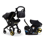 A Doona Car Seat and Stroller from the Midnight Edition, featuring a black design with yellow accents, is shown with a matching detachable infant car seat. A black quilted diaper bag is attached to the stroller handle.