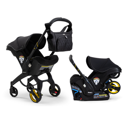 A Doona Car Seat and Stroller from the Midnight Edition, featuring a black design with yellow accents, is shown with a matching detachable infant car seat. A black quilted diaper bag is attached to the stroller handle.