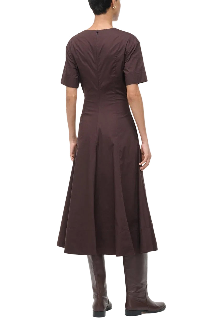 A person is shown from the back wearing the Staud Frances Dress—a short-sleeve, dark brown split neck poplin A-line dress—paired with matching knee-high boots.