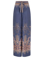 The Zimmermann Valiant Track Pant is a wide-leg, high-rise silk pant with floral and paisley print, drawstring waistband, and elastic front tie in classic navy.