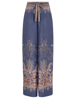The Zimmermann Valiant Track Pant is a wide-leg, high-rise silk pant with floral and paisley print, drawstring waistband, and elastic front tie in classic navy.