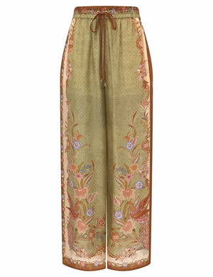 The Indra Relaxed Pant by Zimmermann features wide-leg silk habutae with a green base, brown drawstring waist, and floral patterns on sides and hem.